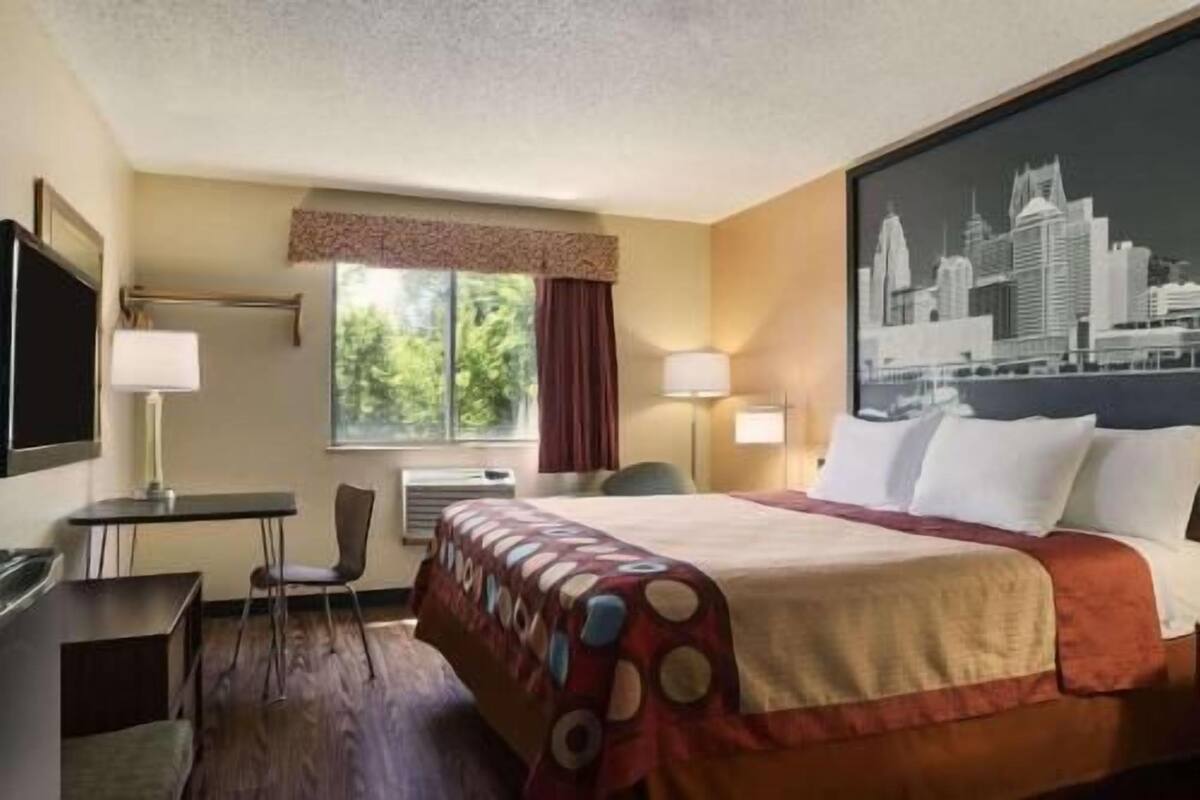 A hotel room with a bed, a desk, a chair, a window with curtains, and a cityscape view.