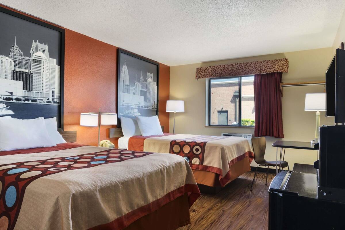 A hotel room with two beds, a desk, and a window with curtains.