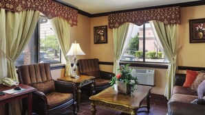 A hotel lobby with a brown leather armchair, a wooden coffee table with a vase of flowers, and a desk with a telephone. - Super 8 by Wyndham Taylor/Detroit Area (Taylor)