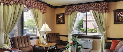 A hotel lobby with a brown leather armchair, a wooden coffee table with a vase of flowers, and a desk with a telephone.