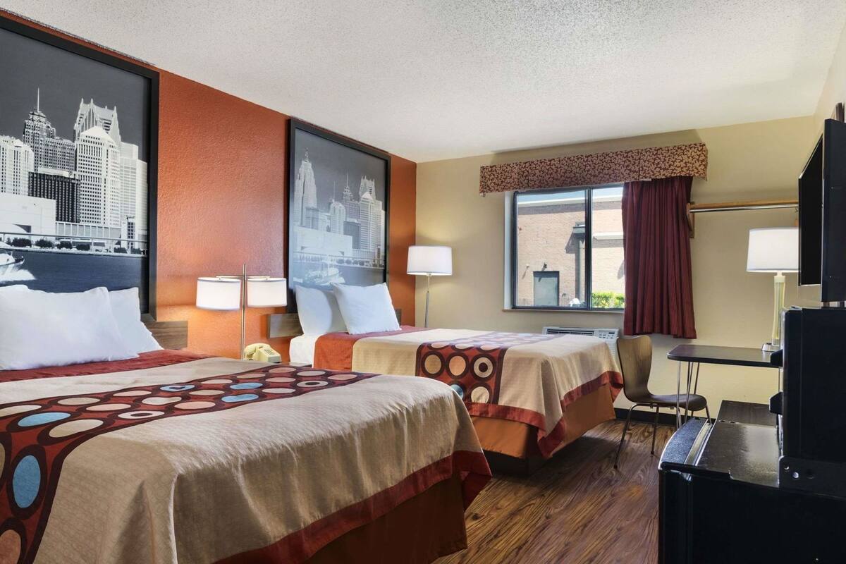 A hotel room with two beds, a desk, a chair, a TV, and two lamps.