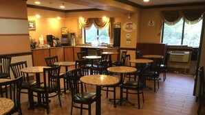 A restaurant with multiple tables and chairs, a counter with a coffee machine, and a view of the outdoors through large windows. - Super 8 by Wyndham Taylor/Detroit Area (Taylor)