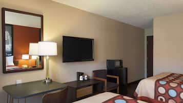 Habitación de hotel con escritorio, una silla, televisor, microondas y dos camas con cubrecamas estampados.