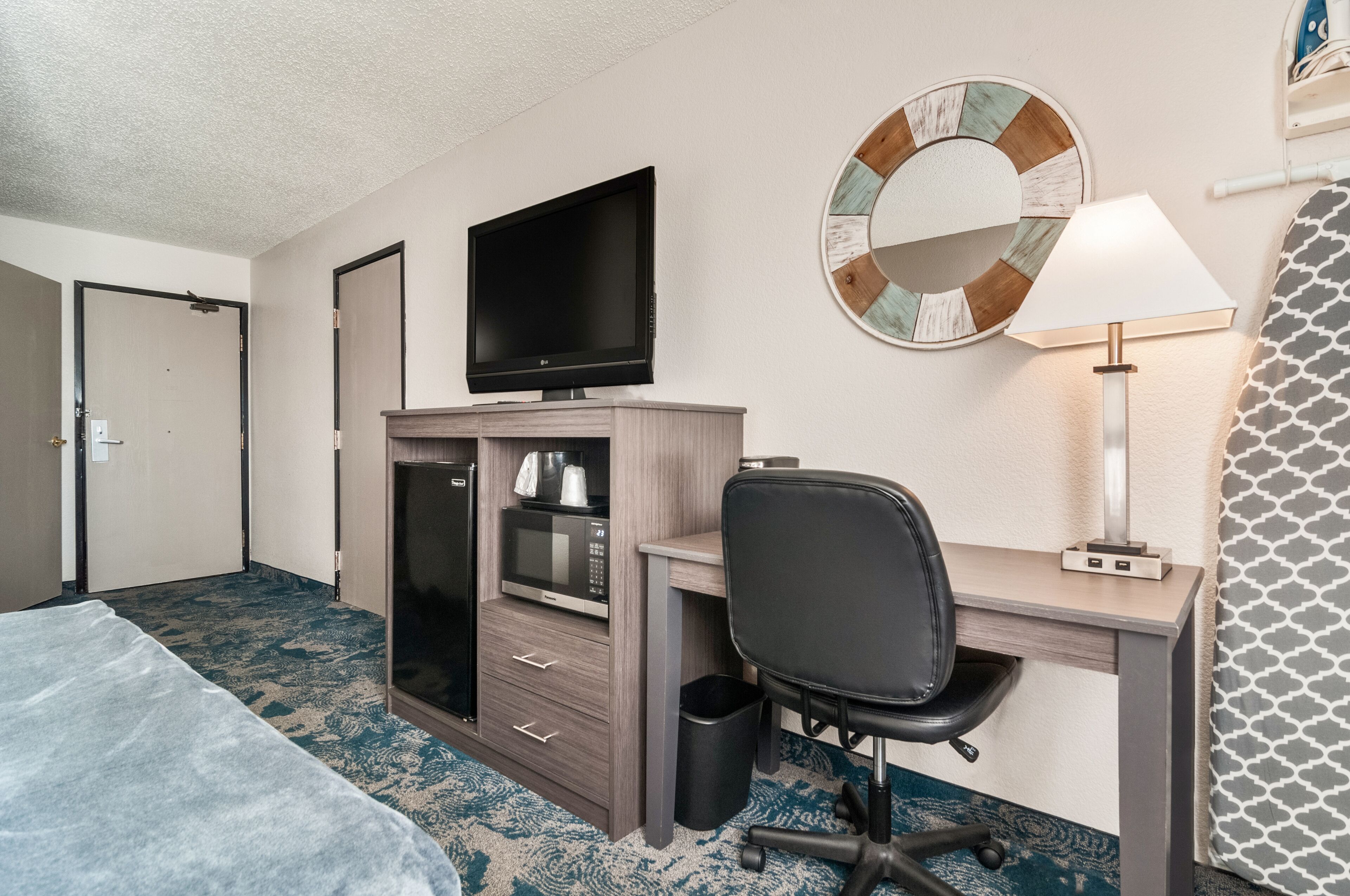 Une chambre d’hôtel équipée d’un lit, d’un bureau avec un ordinateur, d’une télévision, d’un four à micro-ondes et d’une poubelle.