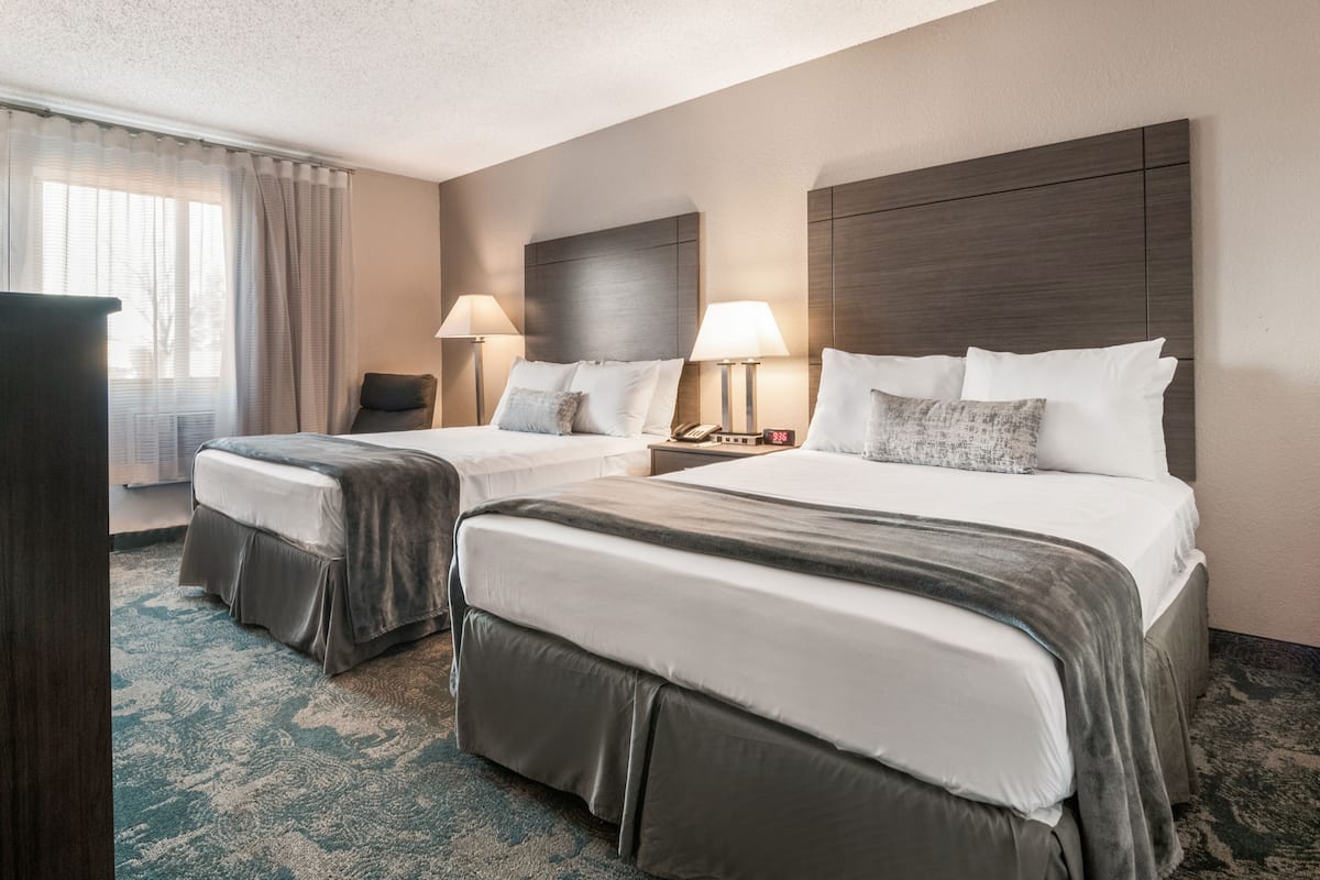 A hotel room with two beds, a desk, and a chair.