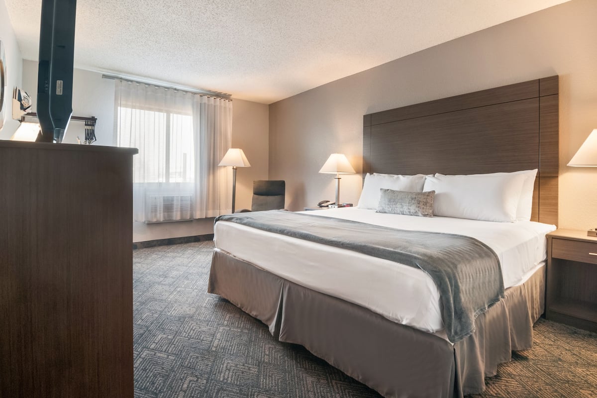 A hotel room with a large bed, two bedside tables, a desk, and a window with curtains.