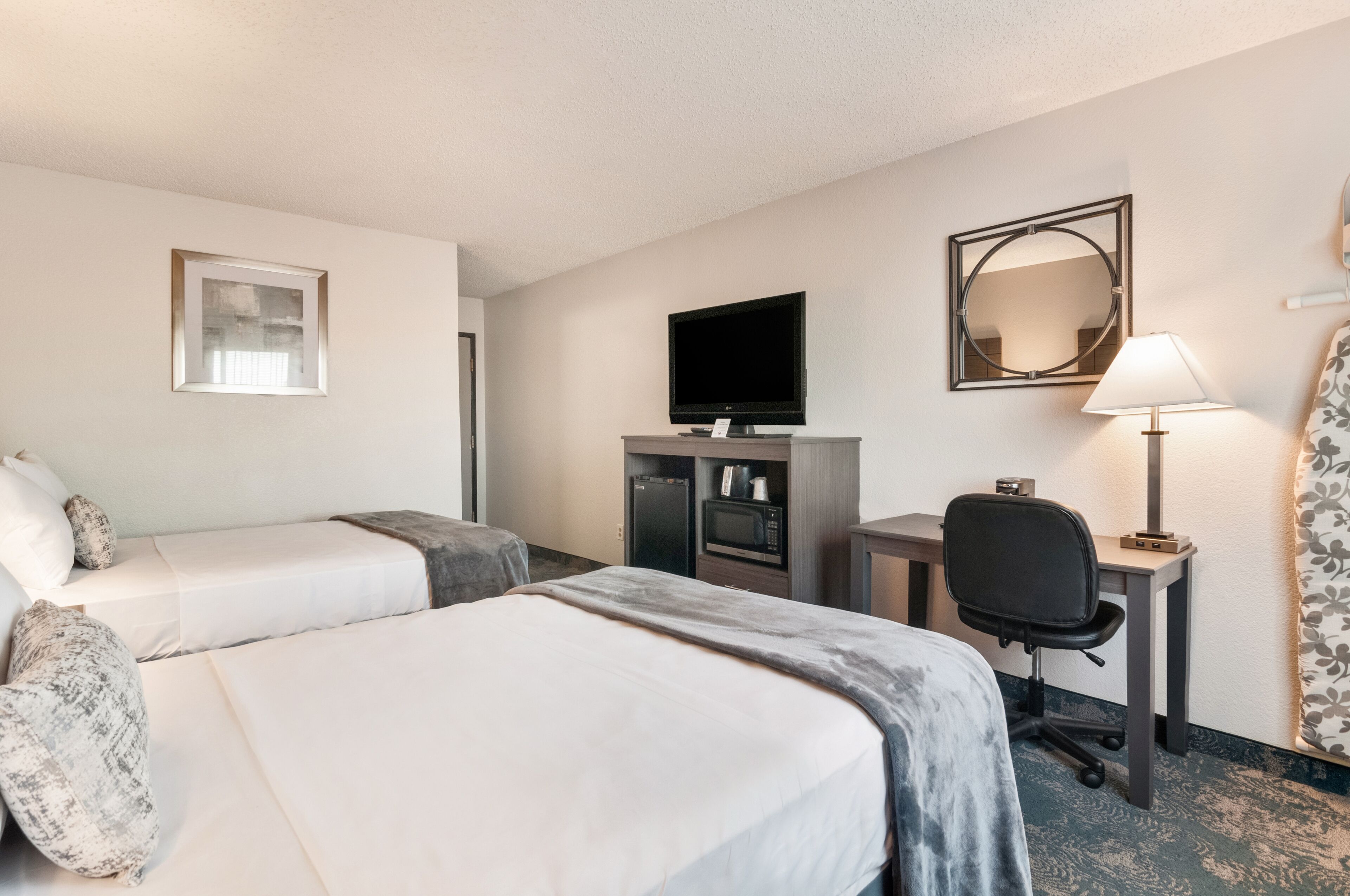 A hotel room with two beds, a desk with a chair, a television, a mirror, and a lamp.