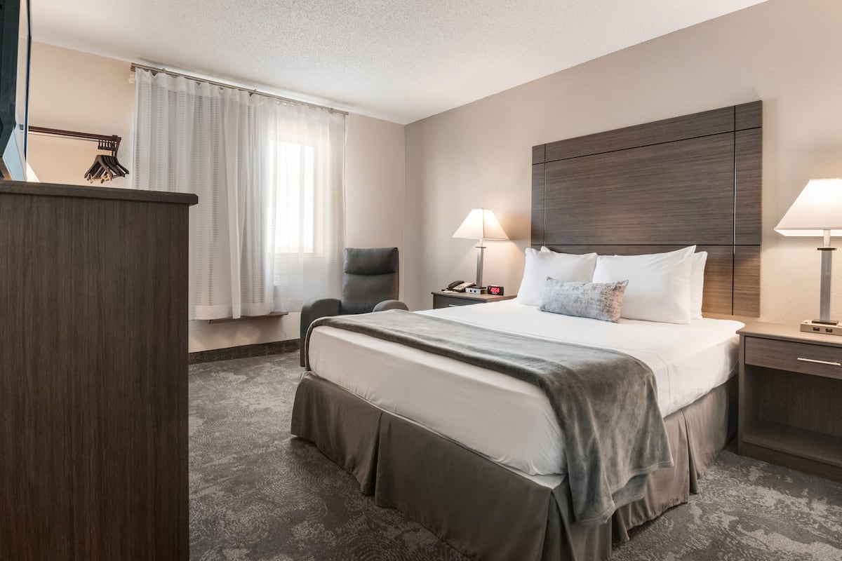 A hotel room with a large bed, bedside tables, a chair, a desk, and a window with curtains.