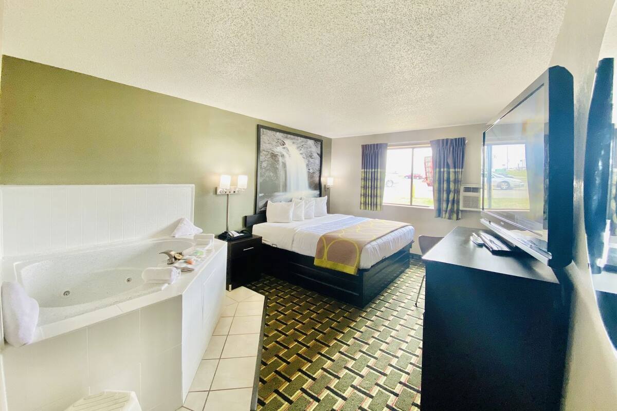 A hotel room with a large bed, a bathtub, a desk, and a television.