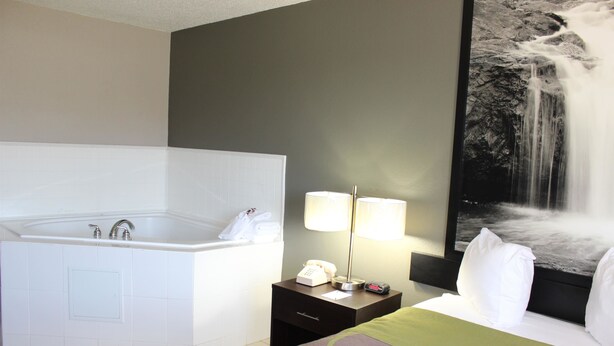 A hotel room with a large bathtub, a bedside table with a lamp, and a wall-mounted TV displaying a waterfall scene. - Super 8 by Wyndham Wyoming/Grand Rapids Area (Wyoming)