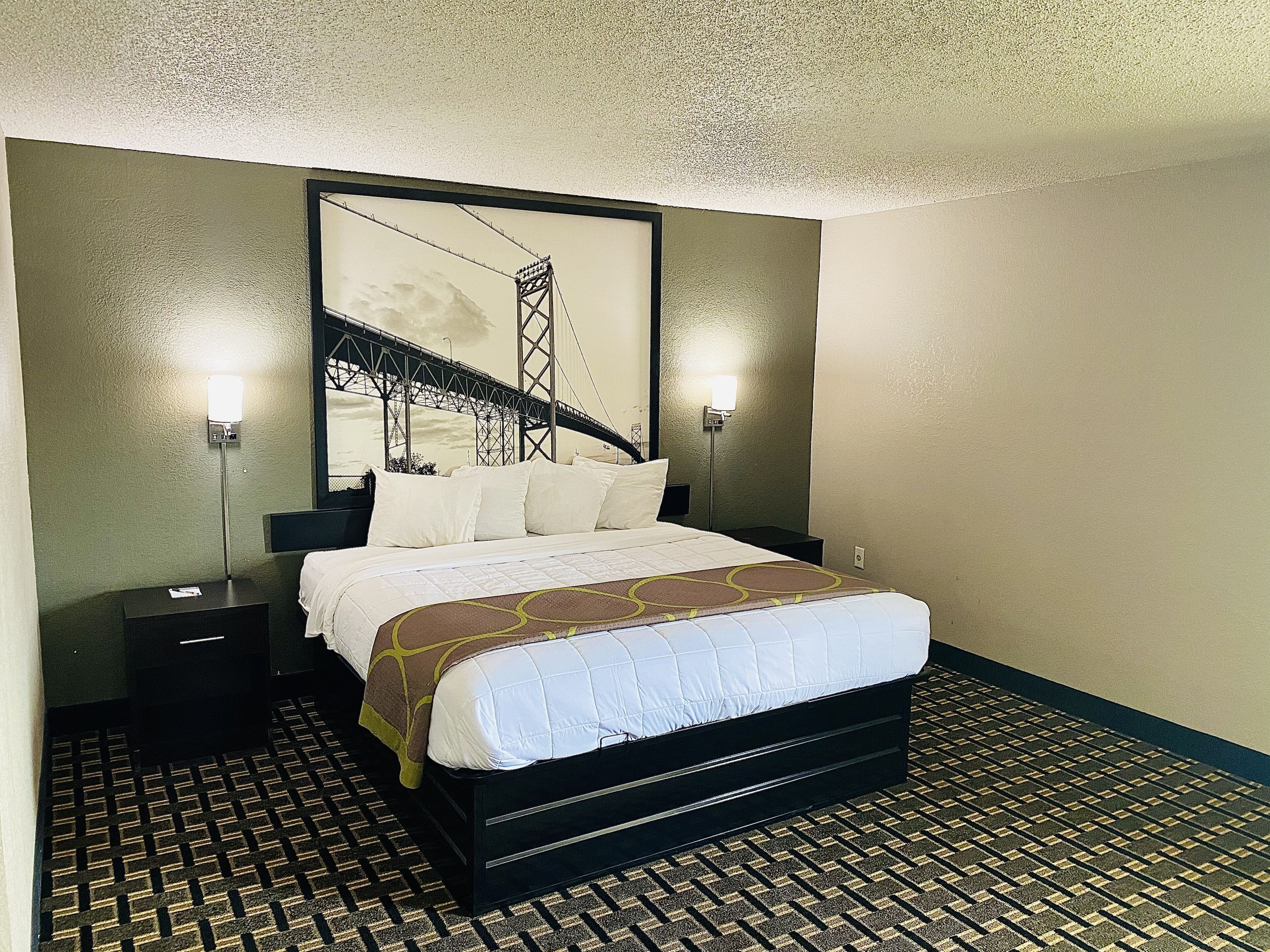 Habitación de hotel con una cama grande, dos mesitas de noche y una obra de arte colgada en la pared que representa un puente.