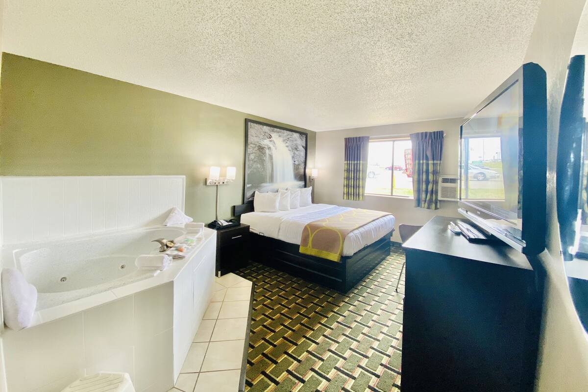 A hotel room with a large bed, a separate bathroom with a bathtub, a desk, and a television.
