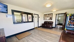 A lobby with a brown leather sofa, a vending machine, a framed welcome sign, and a television mounted on the wall. - Super 8 by Wyndham Wyoming/Grand Rapids Area (Wyoming)