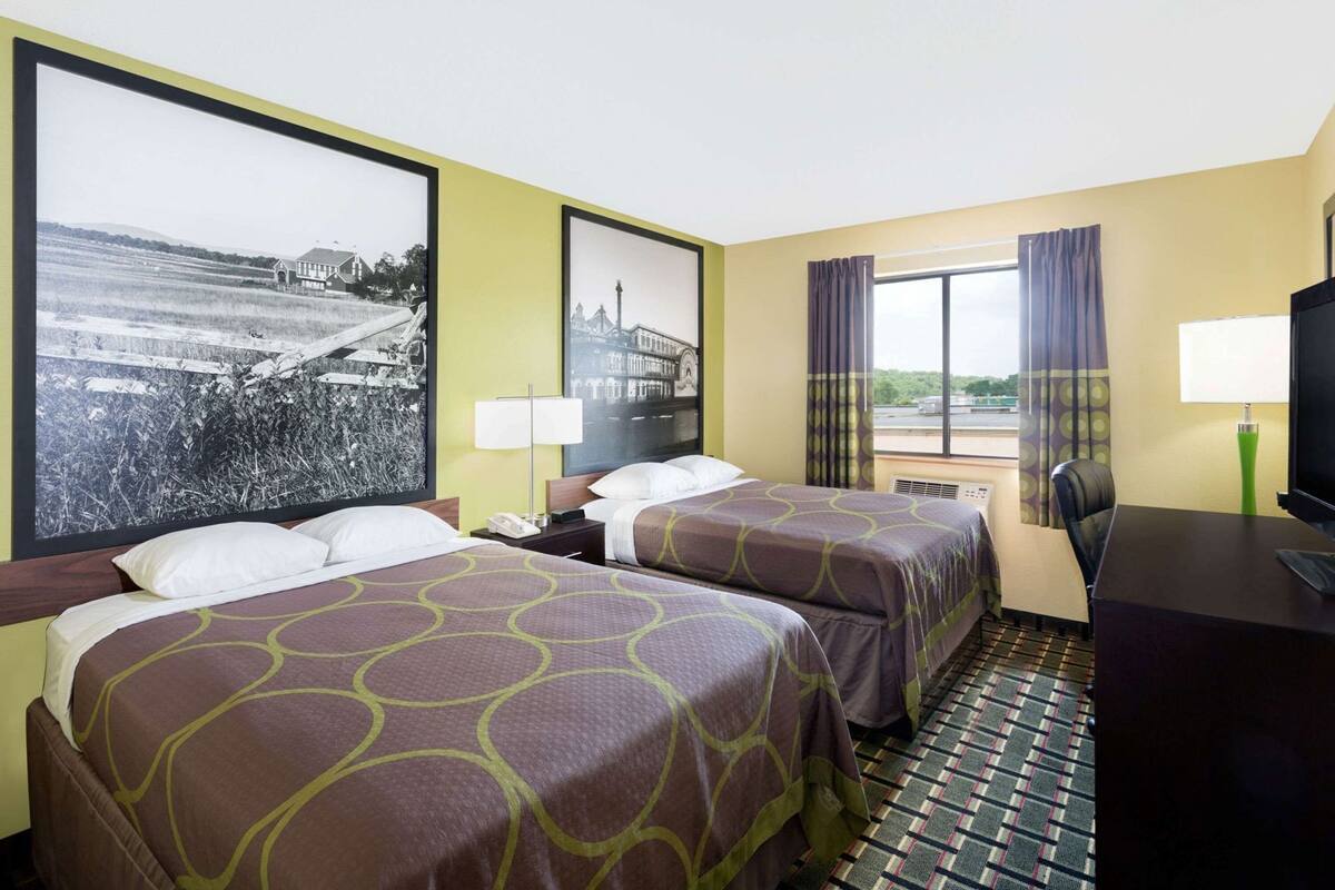 Une chambre d’hôtel avec deux lits, un bureau, une télévision et de grandes fenêtres.