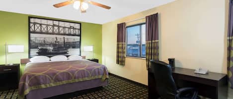 A hotel room with a bed, desk, chair, and a large window with curtains.