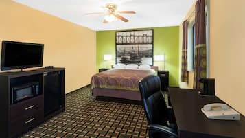 Quarto de hotel com cama, escrivaninha com telefone, televisão, micro-ondas e ventoinha no teto.