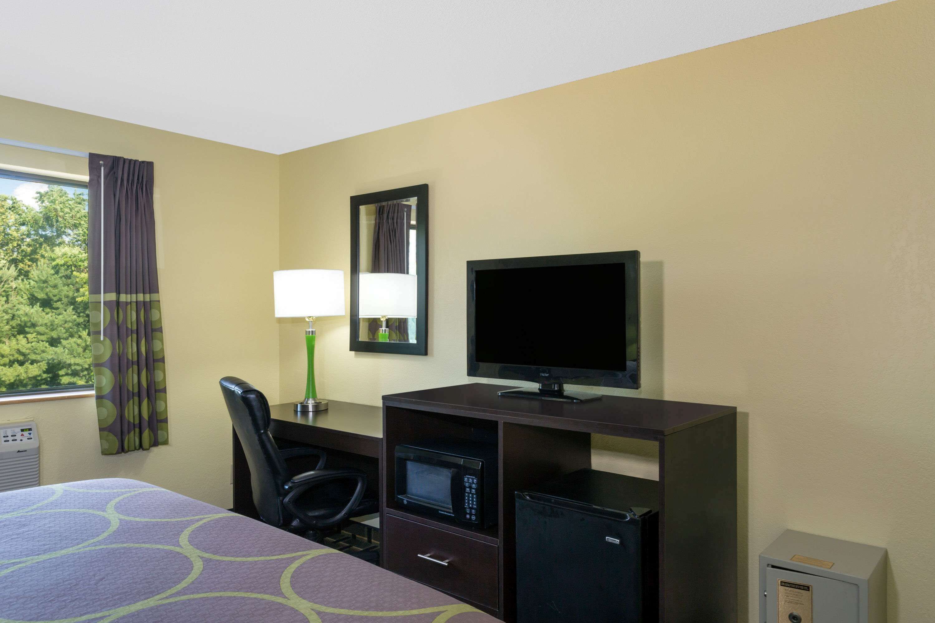 Una habitación de hotel con cama, escritorio, computadora, televisor, microondas y caja fuerte.