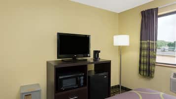 A hotel room with a bed, a TV, a microwave, a refrigerator, a lamp, and a window with curtains.