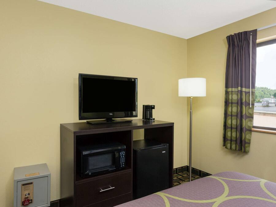 A hotel room with a bed, a TV, a microwave, a refrigerator, a lamp, and a window with curtains.