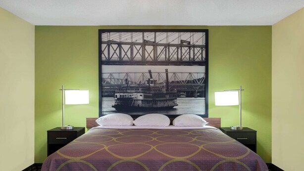 A hotel room with a bed, two nightstands, and a large framed picture of a bridge and boat on the wall. - Super 8 by Wyndham Marietta (Marietta)