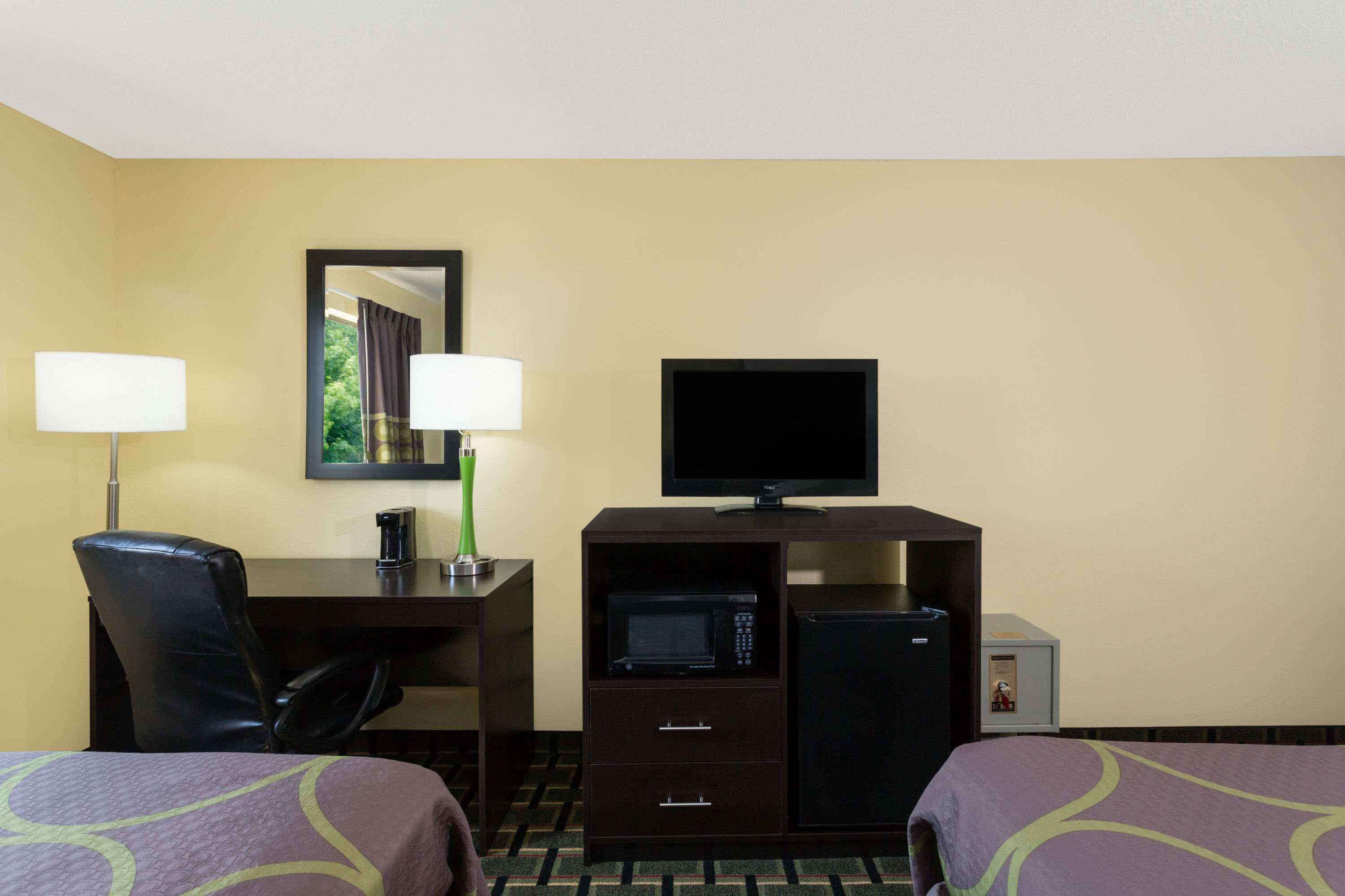 A hotel room with two beds, a desk with a computer, a television, a microwave, and a small refrigerator.