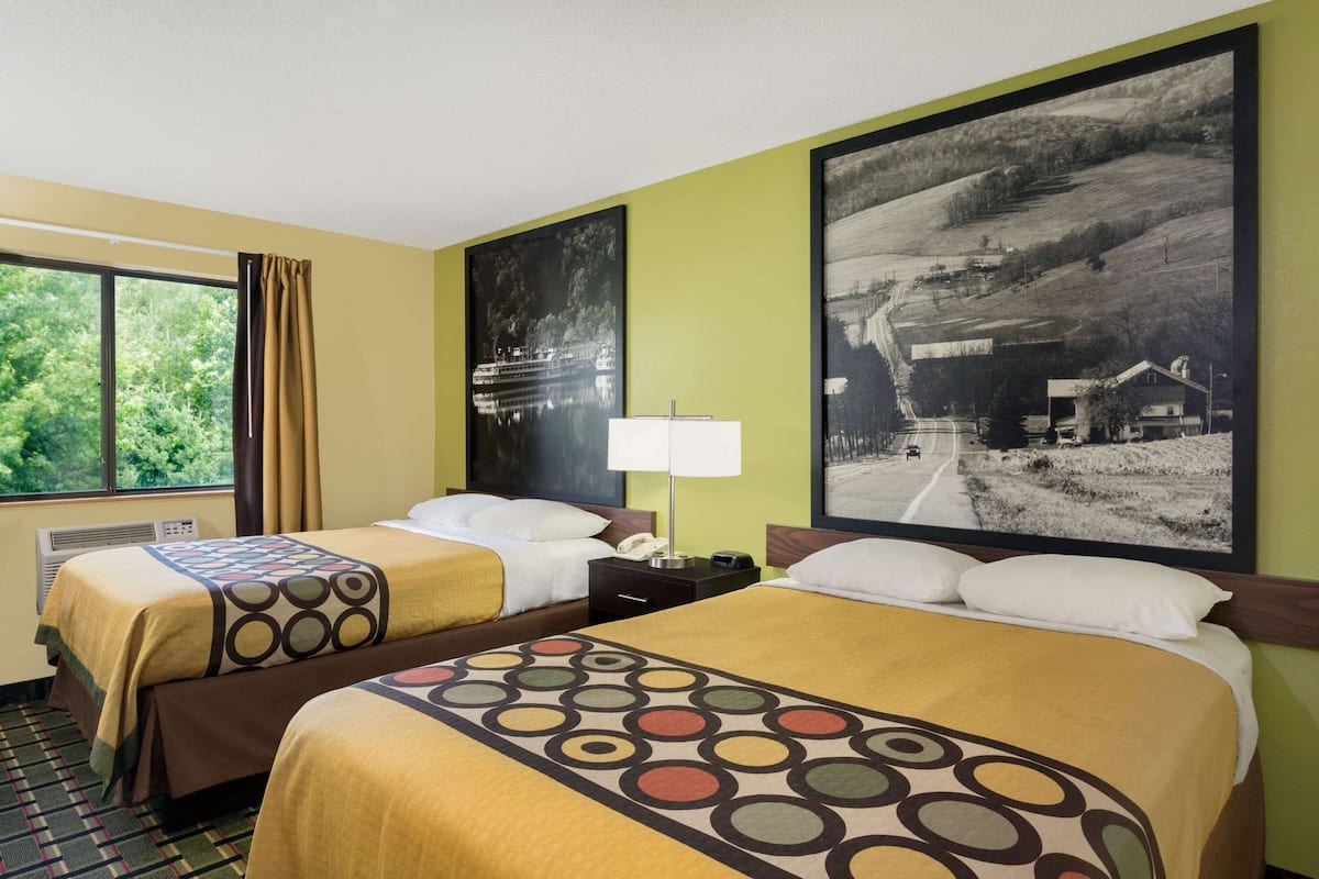 Une chambre d’hôtel avec deux lits, une fenêtre avec des rideaux, une lampe et deux grandes photographies de paysages accrochées au mur.