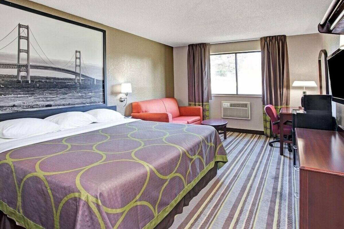 Een hotelkamer met een groot bed, een bureau, een stoel, een televisie en een raam met gordijnen.