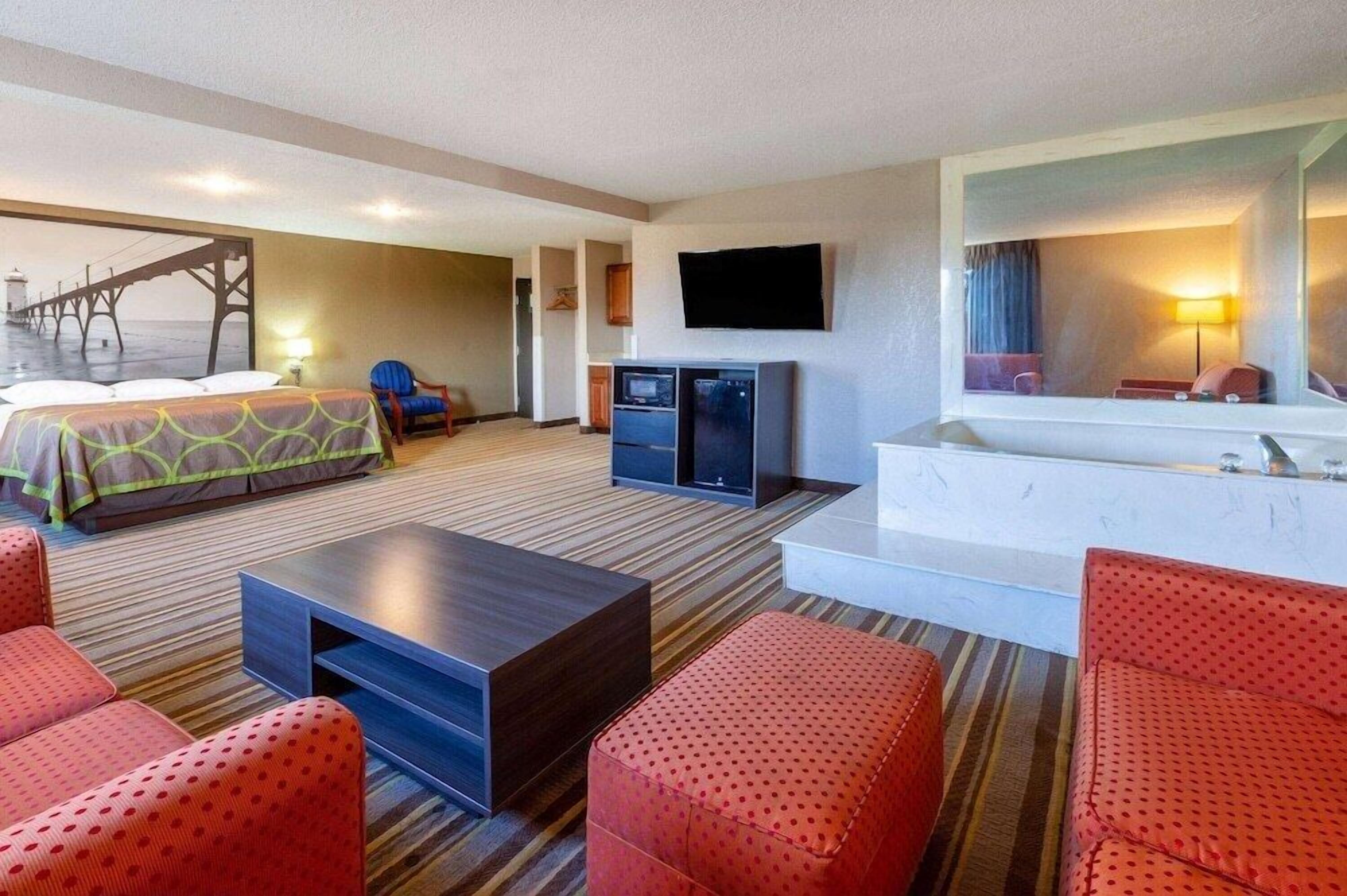 Quarto de hotel com cama, televisão, escrivaninha, cadeira, sofá, pequena cozinha e banheiro.