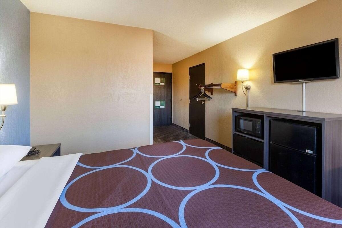 Hotelkamer met een bed, een televisie, een bureau, een kast en een gang naar een deur.