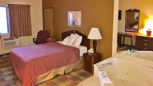 A hotel room with a bed, a desk, a chair, a lamp, a mirror, and a bathtub. - Americas Best Value Inn Livonia Detroit (Livonia)