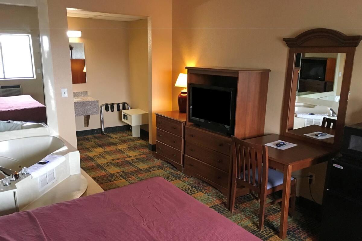 A hotel room with a bed, a desk, a television, a dresser, a mirror, a lamp, and a bathroom with a sink and a bathtub.