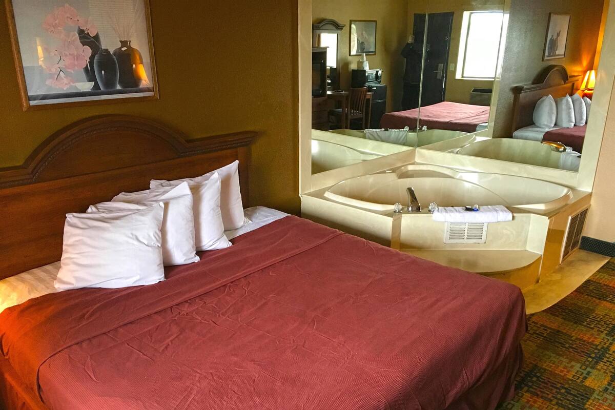 A hotel room with a bed, a large mirror, a desk, and a bathroom with a bathtub.