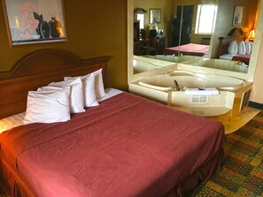 A hotel room with a bed, a large mirror, a desk, and a bathroom with a bathtub. - Americas Best Value Inn Livonia Detroit (Livonia)