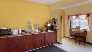 A kitchen with a wooden countertop, a dining table with chairs, and a window with curtains. - Americas Best Value Inn Livonia Detroit (Livonia)