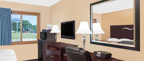 Quarto de hotel com uma cama, uma escrivaninha com cadeira, uma televisão, duas luminárias e um espelho grande.