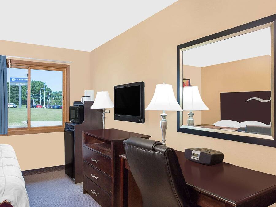 A hotel room with a bed, a desk with a chair, a television, two lamps, and a large mirror.