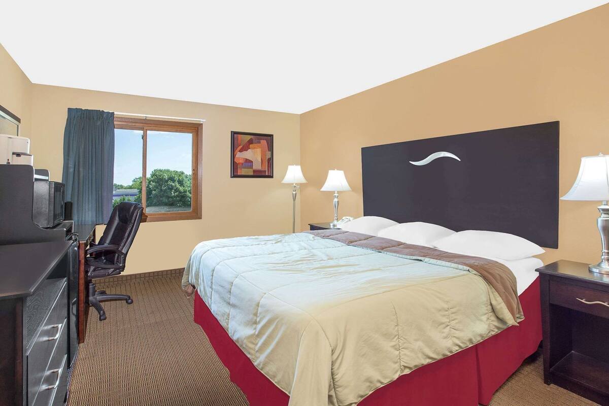 A hotel room with a bed, desk, chair, and two bedside lamps.
