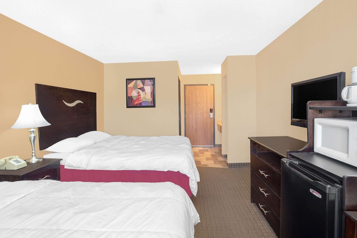 A hotel room with two beds, a television, a refrigerator, a microwave, a telephone, and a painting on the wall.