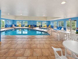 A swimming pool area with tiled flooring, lounge chairs, and a table with chairs.