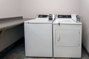 Dos lavadoras blancas de carga frontal en un lavadero pequeño con encimera de granito y suelo de baldosas.