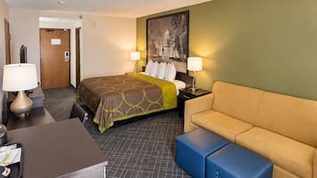 A hotel room with a bed, a sofa, a desk, and a trash bin.