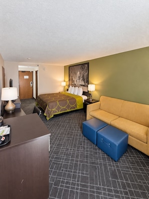 A hotel room with a bed, a sofa, a desk, and a trash bin.