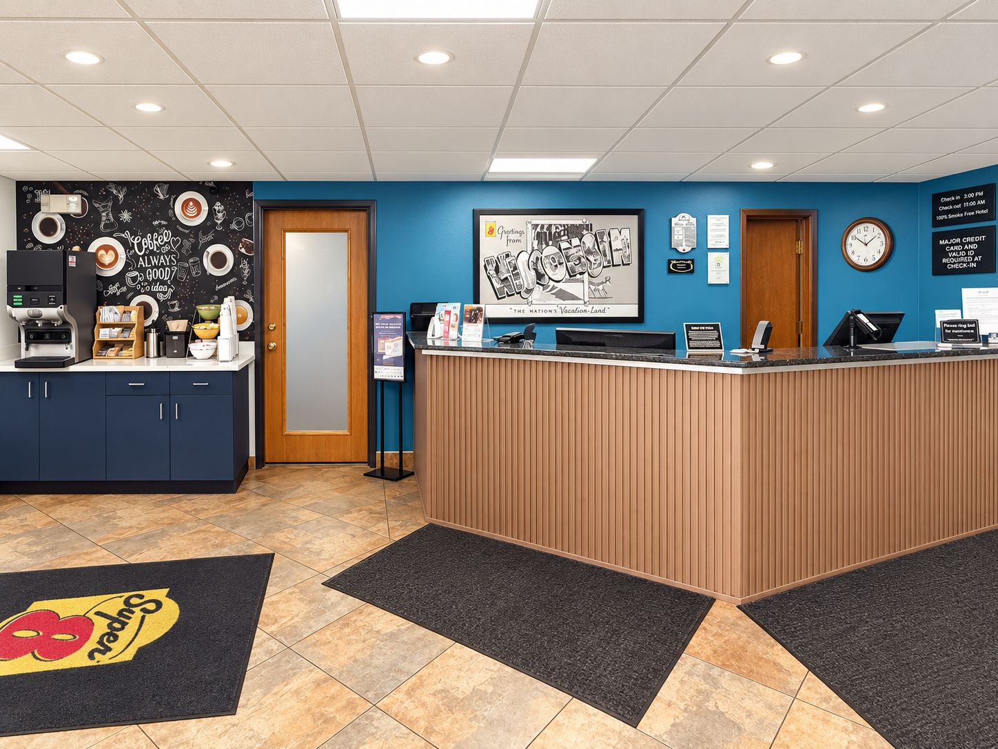 A hotel reception area with a coffee station, a clock, and a framed welcome sign.