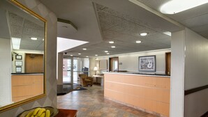 A hotel lobby with a reception desk, a large mirror, a bowl of bananas, and a tiled floor. - Super 8 by Wyndham Madison South (Madison)