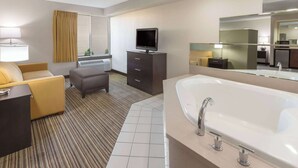 A hotel room with a large bathtub, a television on a dresser, a sofa, and a small table. - Super 8 by Wyndham Madison South (Madison)