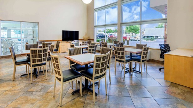 A spacious dining area with multiple tables and chairs, large windows offering a view of the parking lot, and a flat-screen TV mounted on the wall. - Super 8 by Wyndham Madison South (Madison)