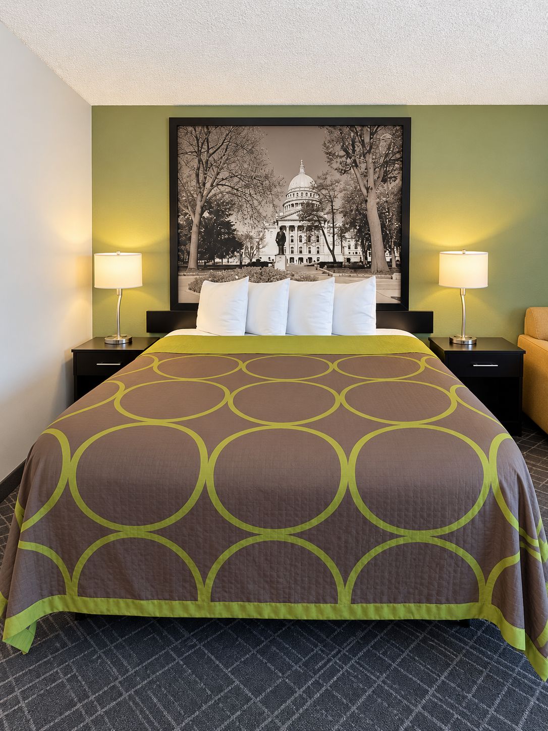 A hotel room with a large bed, two bedside tables with lamps, a framed picture of a building, and a green wall.