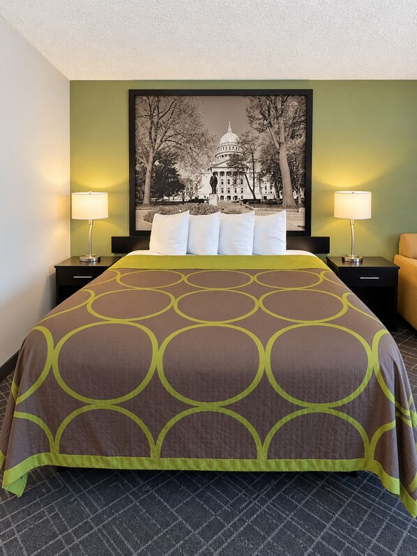 A hotel room with a large bed, two bedside tables with lamps, a framed picture of a building, and a green wall.