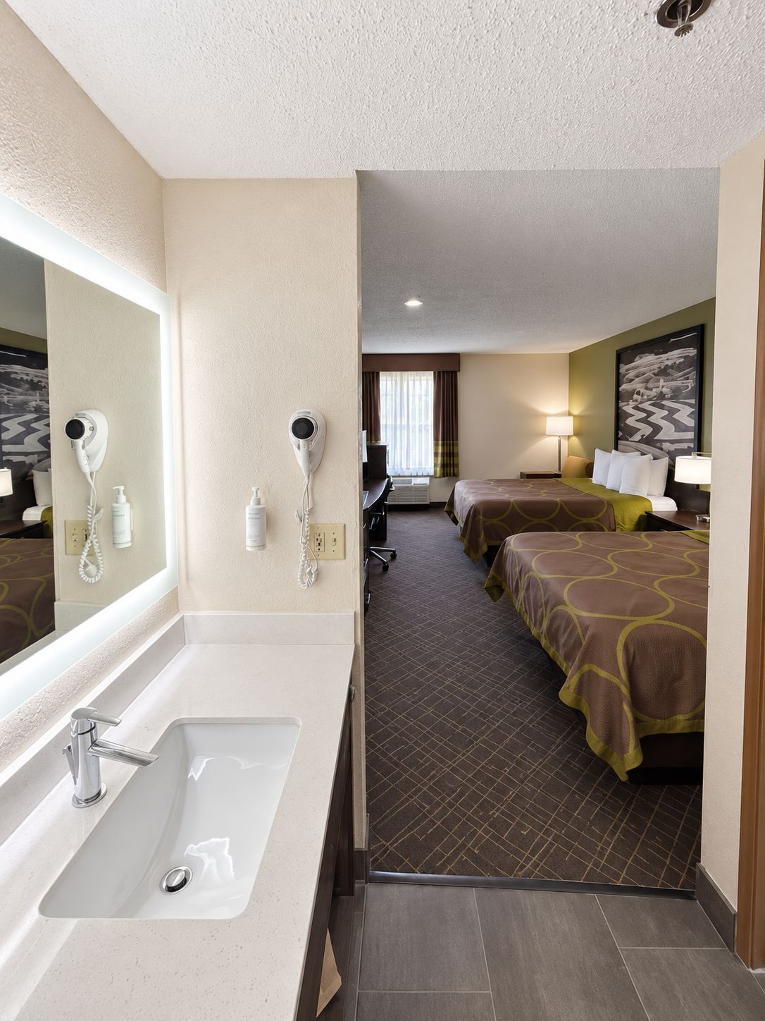 A hotel room with a large bathroom sink, two beds with matching headboards, a mirror, and a painting on the wall.
