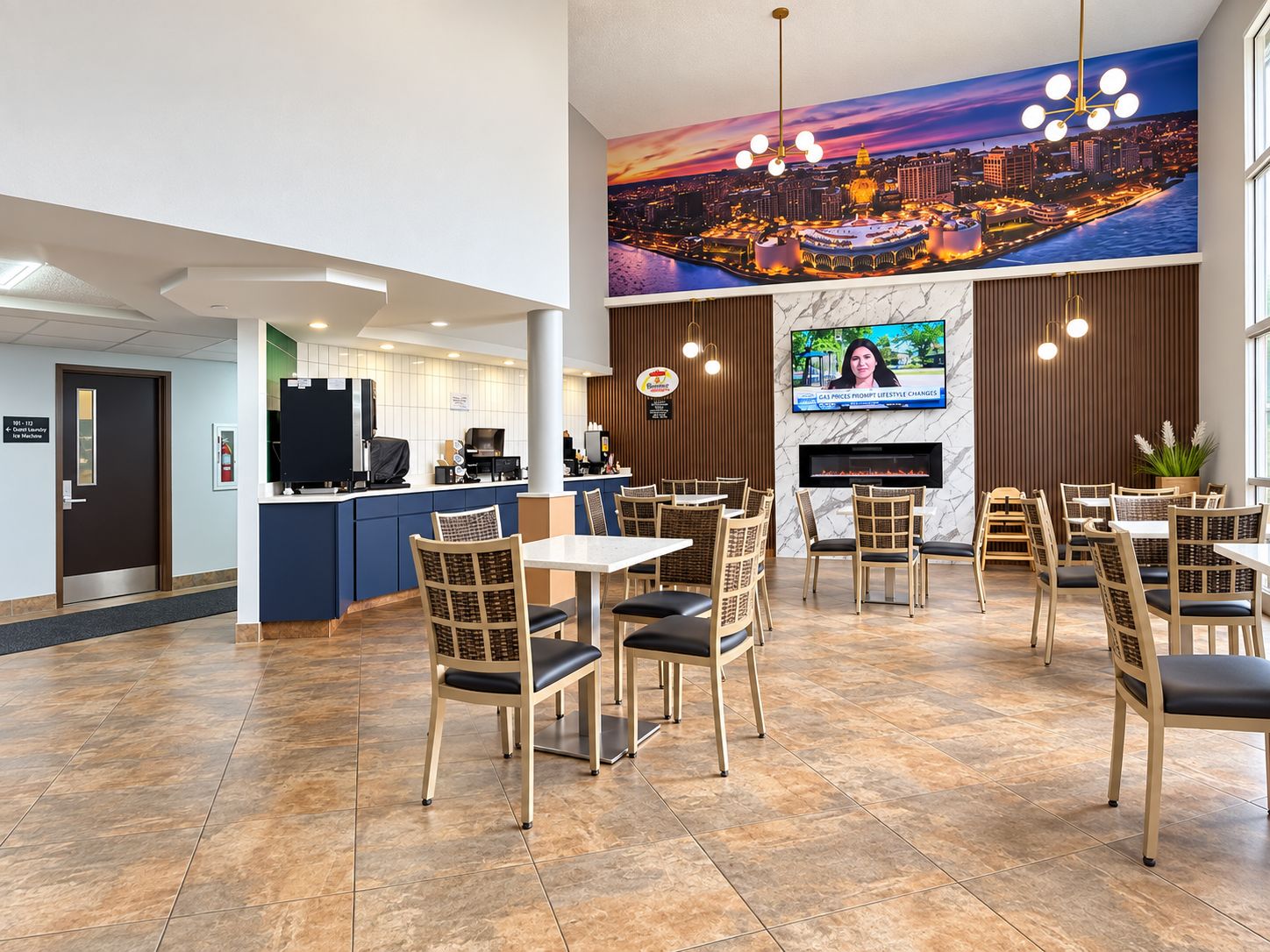 Un vestíbulo de hotel con mostrador de recepción, zona de comedor con mesas y sillas, un gran mural con vista a la ciudad y una pantalla de televisión.